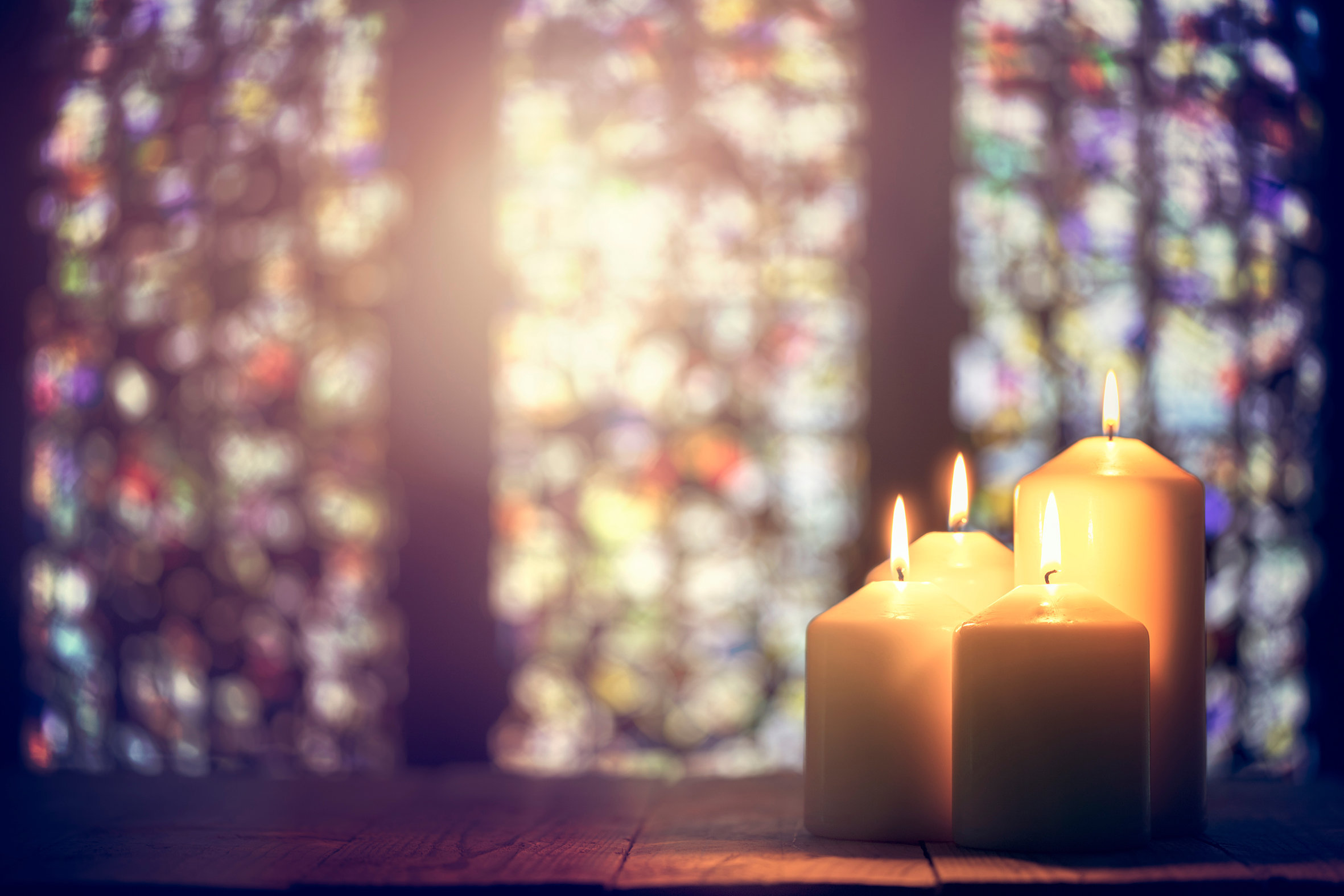 Photograph of candles placed in front of Church stained glass windows
